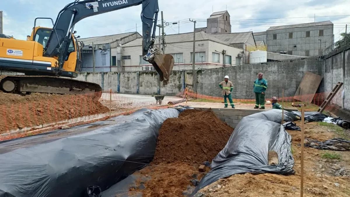 Escavadeira abrindo as valas do sistema, já forradas com lona, ao lado da unidade industrial